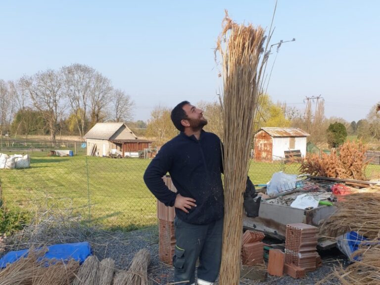 couvreur chaumier portant une botte de roseau sur un chantier en Normandie - Art et Elégance Couverture